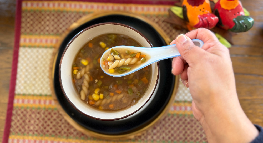 Image of vegan soup with pasta and vegetables served in a bowl, a comforting soup vegan recipe suitable for gluten free food meals.